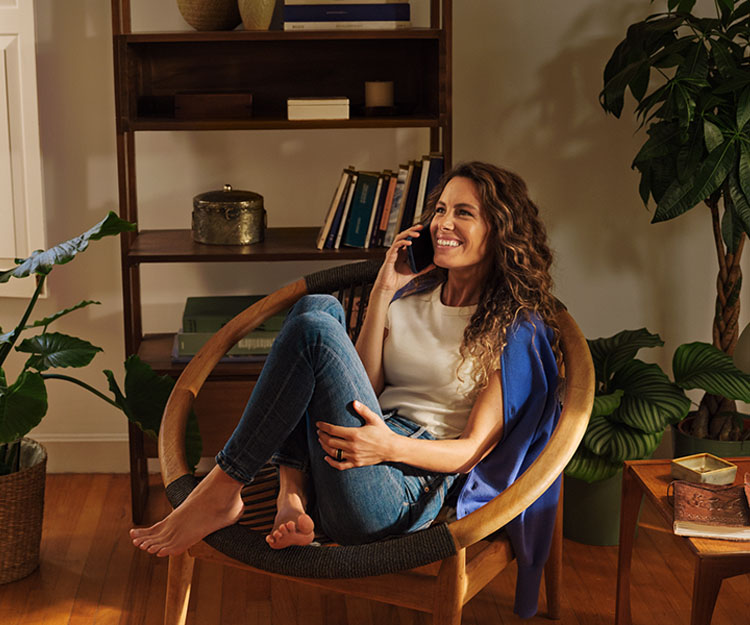chica sonriente, sentada comodamente en una silla moderna, hablando por teléfono