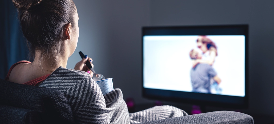 Mujer sentada en el sofá viendo una película mientras come helado