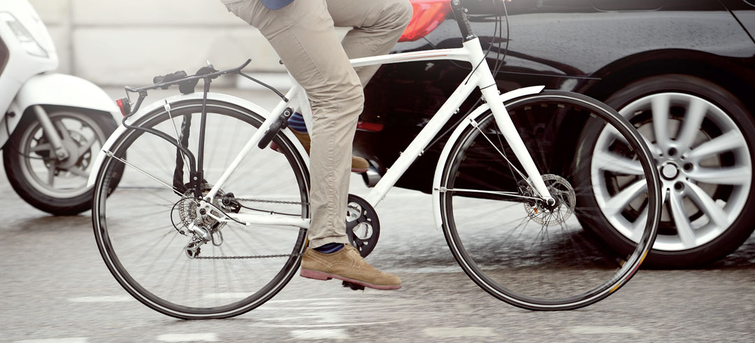 Hombre montado en una bicicleta blanca cerca de un coche y una moto